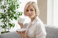 Young beautiful blonde woman in white shirt and glasses is sitting on the sofa in bright office against the window Royalty Free Stock Photo