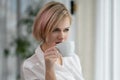 Young beautiful blonde woman in white shirt and glasses is sitting on the sofa in bright office against the window Royalty Free Stock Photo