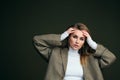 A young beautiful blonde woman in a white turtleneck and a man`s jacket poses on a green olive background in the studio. Royalty Free Stock Photo