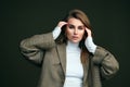 A young beautiful blonde woman in a white turtleneck and a man`s jacket poses on a green olive background in the studio. Royalty Free Stock Photo