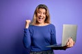 Young beautiful blonde woman working using laptop over isolated purple background pointing and showing with thumb up to the side Royalty Free Stock Photo