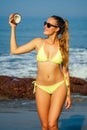 Young and beautiful blonde woman in a yellow swimsuit holding a coconut in her hand on a tropical beach.girl in bikini Royalty Free Stock Photo