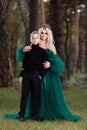 Young beautiful blonde woman queen with young boy in black outfit. Princess mother walks with son. autumn green forest mystic. Royalty Free Stock Photo