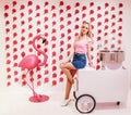 Young beautiful blondie girl posing against a wall background with pink ice cream and equipment for making sweet cotton wool. Swee