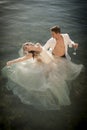 Young beautiful bridal couple dancing in rock pool with glasses