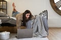 Young beautiful bruenette woman in cozy sweater in bed at home working on a laptop