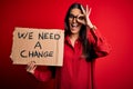 Young beautiful brunette activist woman protesting for a change holding banner with happy face smiling doing ok sign with hand on