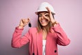 Young beautiful brunette architect woman wearing safety helmet hoding key of house with happy face smiling doing ok sign with hand Royalty Free Stock Photo