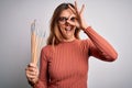 Young beautiful brunette artist woman holding painter brushes over white background with happy face smiling doing ok sign with Royalty Free Stock Photo