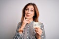 Young beautiful brunette businesswoman overworked holding help reminder paper serious face thinking about question, very confused