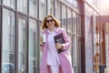 a young beautiful brunette businesswoman in sunglasses and a pink coat is walking along a city street Royalty Free Stock Photo