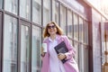 a young beautiful brunette businesswoman in sunglasses and a pink coat is walking along a city street, in her hands she has a Royalty Free Stock Photo