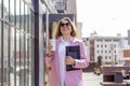 a young beautiful brunette businesswoman in sunglasses and a pink coat is walking along a city street Royalty Free Stock Photo