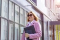 a young beautiful brunette businesswoman in sunglasses and a pink coat is walking along a city street Royalty Free Stock Photo