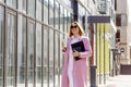 a young beautiful brunette businesswoman in sunglasses and a pink coat is walking along a city street Royalty Free Stock Photo