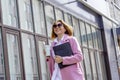 a young beautiful brunette businesswoman in sunglasses and a pink coat is walking along a city street Royalty Free Stock Photo