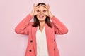 Young beautiful brunette businesswoman wearing elegant jacket over isolated pink background doing ok gesture like binoculars Royalty Free Stock Photo