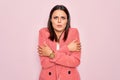 Young beautiful brunette businesswoman wearing elegant jacket over isolated pink background shaking and freezing for winter cold