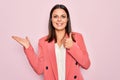 Young beautiful brunette businesswoman wearing elegant jacket over isolated pink background Showing palm hand and doing ok gesture Royalty Free Stock Photo