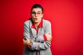 Young beautiful brunette businesswoman wearing jacket and glasses over red background shaking and freezing for winter cold with