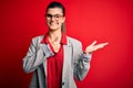 Young beautiful brunette businesswoman wearing jacket and glasses over red background Showing palm hand and doing ok gesture with Royalty Free Stock Photo