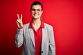 Young beautiful brunette businesswoman wearing jacket and glasses over red background smiling looking to the camera showing Royalty Free Stock Photo