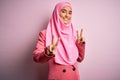 Young beautiful brunette businesswoman wearing pink muslim hijab and business jacket smiling looking to the camera showing fingers Royalty Free Stock Photo