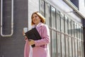 a young beautiful brunette businesswoman in a white blouse and light trousers and a pink coat is walking along a city street Royalty Free Stock Photo