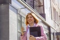 a young beautiful brunette businesswoman in a white blouse and light trousers and a pink coat is walking along a city Royalty Free Stock Photo