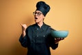 Young beautiful brunette chef woman wearing cooker uniform and hat holding bowl and whisk pointing and showing with thumb up to Royalty Free Stock Photo