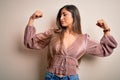 Young beautiful brunette elegant woman with long hair standing over isolated background showing arms muscles smiling proud Royalty Free Stock Photo