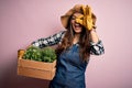 Young beautiful brunette farmer woman wearing apron and hat holding box with plants with happy face smiling doing ok sign with Royalty Free Stock Photo