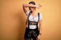 Young beautiful brunette german woman celebrating Octoberfest wearing traditional dress covering eyes with arm, looking serious