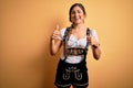 Young beautiful brunette german woman celebrating Octoberfest wearing traditional dress success sign doing positive gesture with