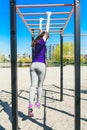 Young beautiful brunette girl in blue t-shirt climbing a horizontal ladder in the park. Royalty Free Stock Photo