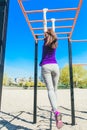 Young beautiful brunette girl in blue t-shirt climbing a horizontal ladder in the park. Royalty Free Stock Photo