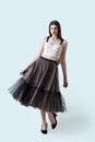 Young beautiful brunette girl in waving dark box pleated midi skirt posing in studio. Woman dancing or making a step.