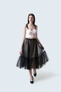 Young beautiful brunette girl in waving dark box pleated midi skirt posing in studio. Woman dancing or making a step.