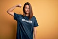 Young beautiful brunette girl doing volunteering wearing t-shirt with volunteer message word Strong person showing arm muscle,