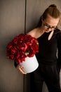 Young beautiful brunette girl standing near wall with big round box of red peony flowers Royalty Free Stock Photo