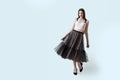 Young beautiful brunette girl in waving dark box pleated midi skirt posing in studio. Woman dancing or making a step.