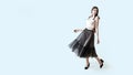 Young beautiful brunette girl in waving dark box pleated midi skirt posing in studio. Woman dancing or making a step.