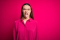 Young beautiful brunette girl wearing casual shirt standing over isolated pink background sticking tongue out happy with funny Royalty Free Stock Photo