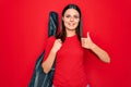 Young beautiful brunette guitarist woman holding guitar case over isolated red background Smiling happy and positive, thumb up Royalty Free Stock Photo