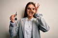 Young beautiful brunette house agent woman holding key home over white background with happy face smiling doing ok sign with hand Royalty Free Stock Photo