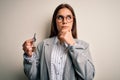 Young beautiful brunette house agent woman holding key home over white background serious face thinking about question, very Royalty Free Stock Photo