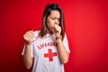Young beautiful brunette lifeguard girl wearing t-shirt with red cross using whistle feeling unwell and coughing as symptom for