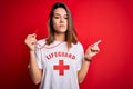 Young beautiful brunette lifeguard girl wearing t-shirt with red cross using whistle Pointing with hand finger to the side showing