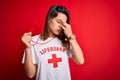 Young beautiful brunette lifeguard girl wearing t-shirt with red cross using whistle tired rubbing nose and eyes feeling fatigue