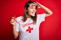 Young beautiful brunette lifeguard girl wearing t-shirt with red cross using whistle very happy and smiling looking far away with